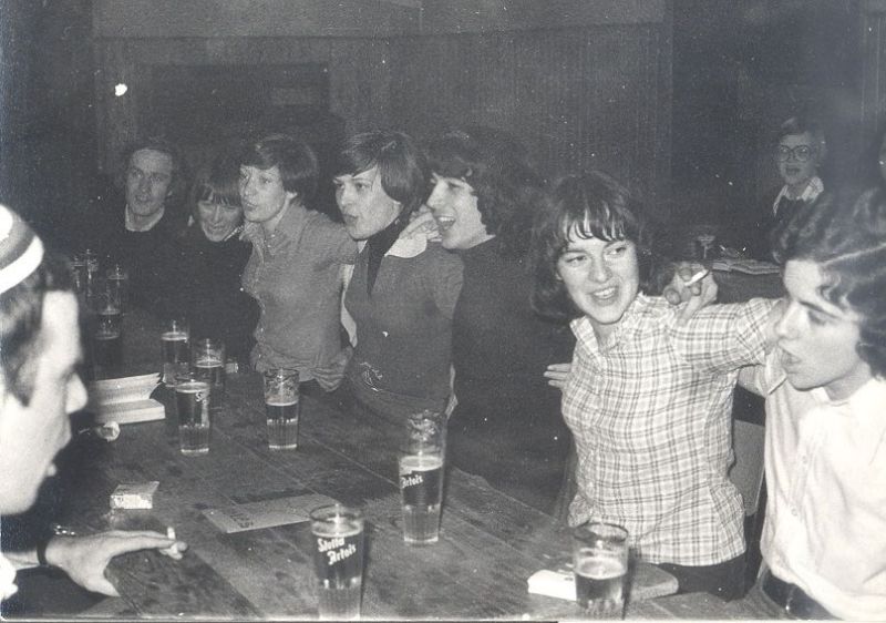 Zwart-witfoto van studenten aan een lange tafel met pinten